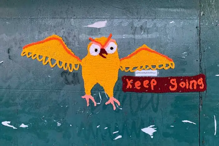 A yarnbomb of an orange owl and a banner that says "Keep Going."